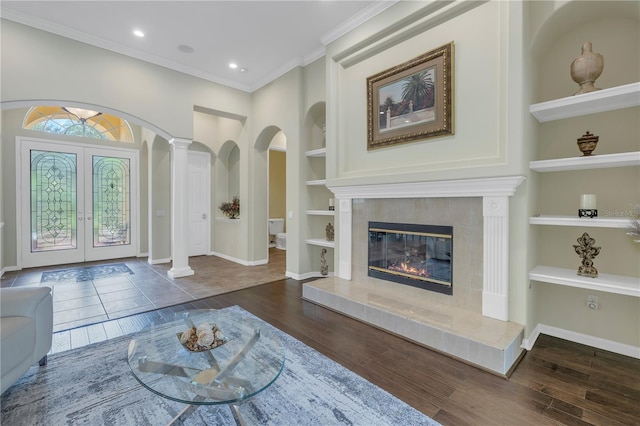 living area featuring built in features, wood finished floors, french doors, ornate columns, and ornamental molding
