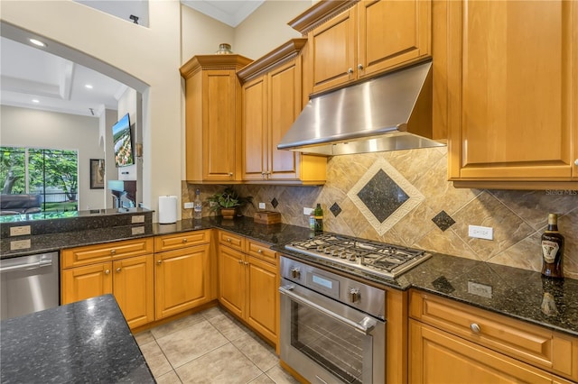 kitchen with appliances with stainless steel finishes, under cabinet range hood, tasteful backsplash, dark stone counters, and ornamental molding