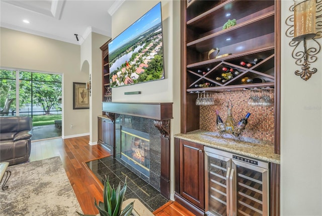 indoor dry bar with crown molding, wine cooler, arched walkways, dark wood-style floors, and baseboards
