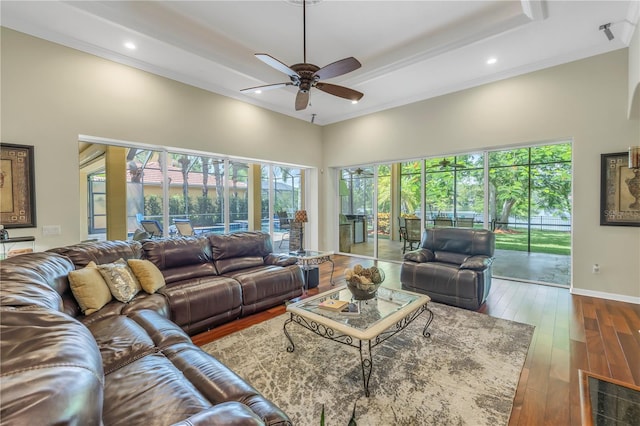 living area with ceiling fan, a towering ceiling, hardwood / wood-style floors, recessed lighting, and baseboards