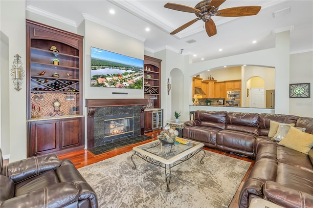 living room with arched walkways, wood finished floors, ceiling fan, ornamental molding, and recessed lighting