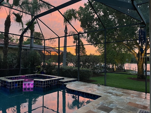 pool at dusk with a lanai, a patio area, a pool with connected hot tub, and a yard