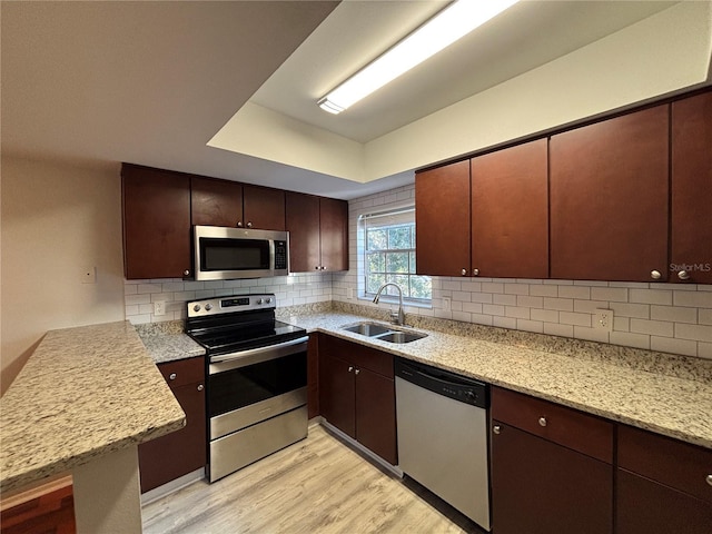 14446 Reuter Strasse Cir Unit 3, Tampa, FL 33613 - kitchen featuring stainless steel appliances, a sink, light wood-style flooring, backsplash, and a peninsula