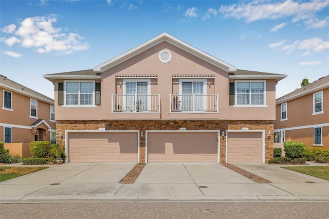 multi unit property with driveway, stone siding, an attached garage, and stucco siding