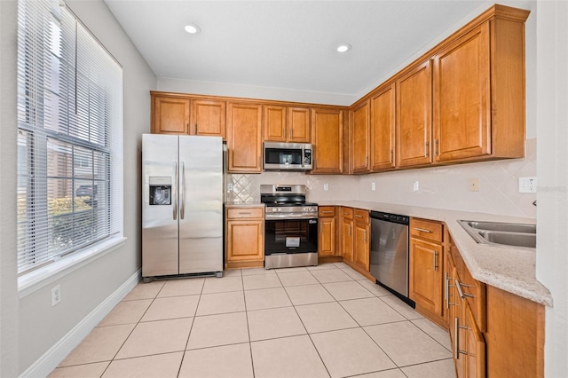 kitchen featuring appliances with stainless steel finishes, a sink, brown cabinets, backsplash, and light tile patterned flooring