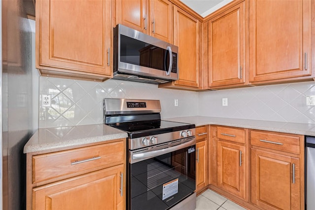kitchen featuring stainless steel appliances, tasteful backsplash, light tile patterned flooring, and light stone counters
