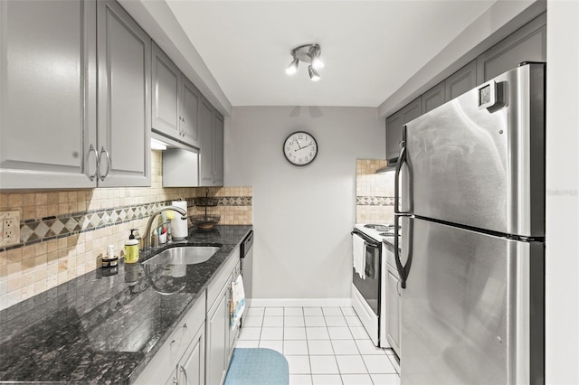 kitchen with appliances with stainless steel finishes, a sink, gray cabinets, light tile patterned floors, and decorative backsplash