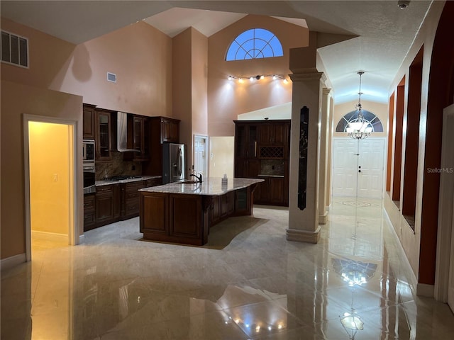 18104 Sweet Jasmine Dr, Tampa, FL 33647 - kitchen with wall chimney range hood, appliances with stainless steel finishes, a chandelier, a center island with sink, and light stone countertops