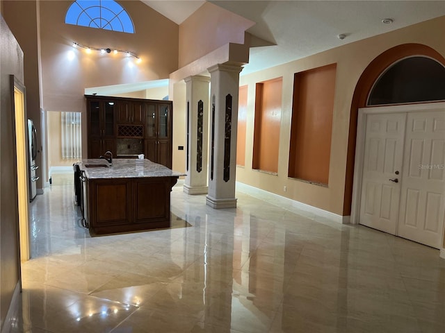 18104 Sweet Jasmine Dr, Tampa, FL 33647 - kitchen featuring decorative columns, light stone counters, an island with sink, glass insert cabinets, and lofted ceiling