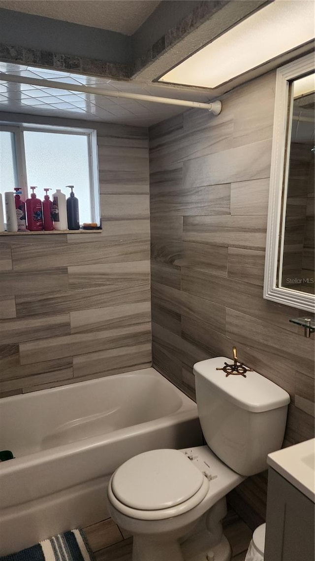 full bathroom featuring toilet, tile walls, a bathtub, and vanity