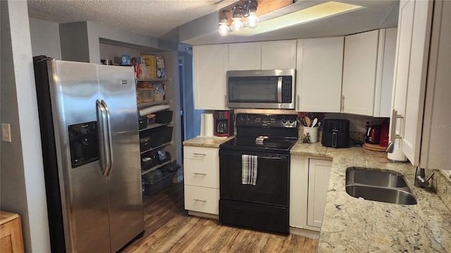 kitchen featuring stainless steel appliances, white cabinetry, a sink, light wood finished floors, and light stone counters