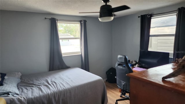 bedroom with light wood-style flooring, ceiling fan, a textured ceiling, and an office area