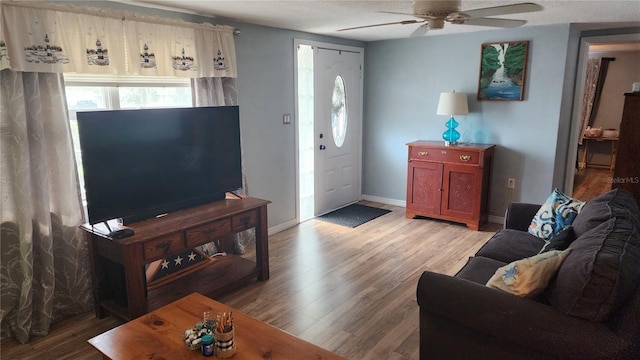 living room with ceiling fan, healthy amount of natural light, light wood-style floors, baseboards, and a textured ceiling