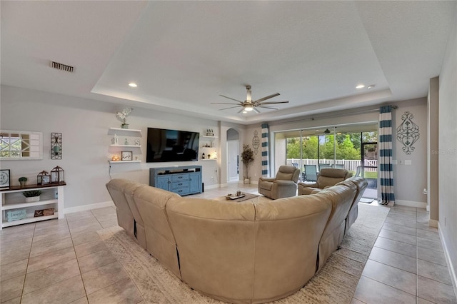 living room featuring a raised ceiling, light tile patterned flooring, arched walkways, baseboards, and recessed lighting