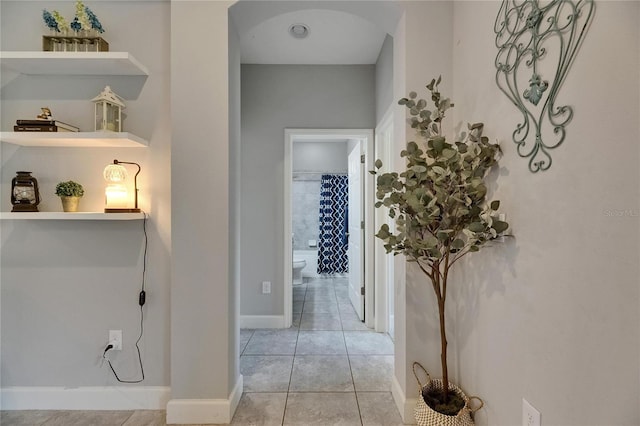 hallway with arched walkways, light tile patterned floors, and baseboards