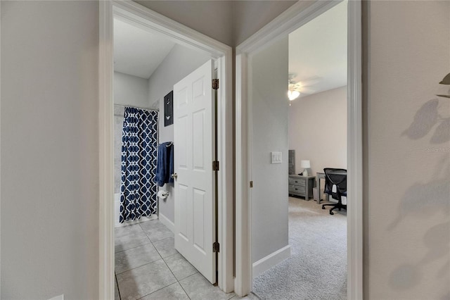 corridor with light tile patterned floors, baseboards, and a desk