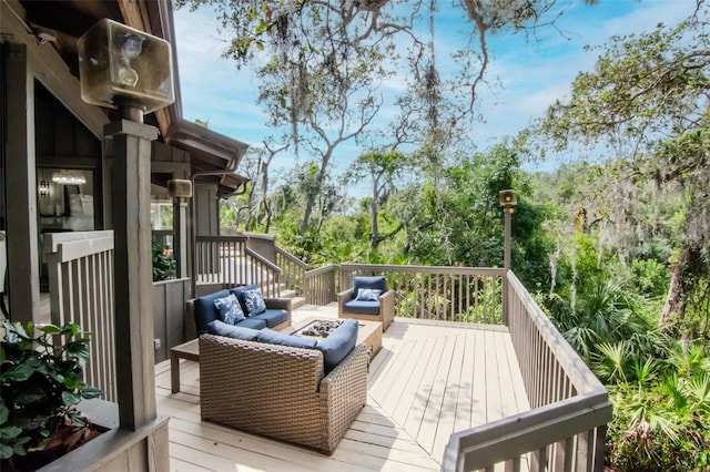 wooden deck featuring an outdoor living space with a fire pit and view of wooded area