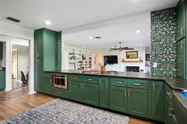 4009 Carrollwood Village Dr, Tampa, FL 33618 - kitchen with green cabinetry, a ceiling fan, light wood-style flooring, a fireplace, and dark countertops