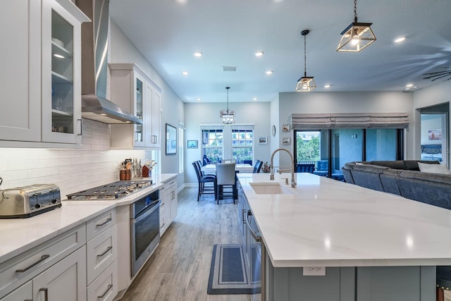 kitchen featuring appliances with stainless steel finishes, a sink, wall chimney exhaust hood, backsplash, and light wood-style floors