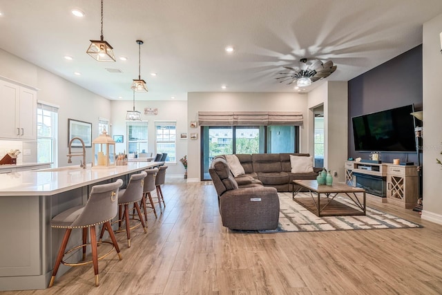 living room featuring light wood-style flooring, recessed lighting, plenty of natural light, ceiling fan, and baseboards