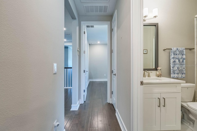 hall featuring dark wood-type flooring, baseboards, and a sink
