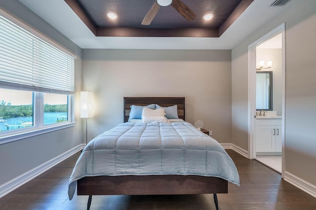 bedroom with wood-type flooring, baseboards, a tray ceiling, ensuite bathroom, and a sink