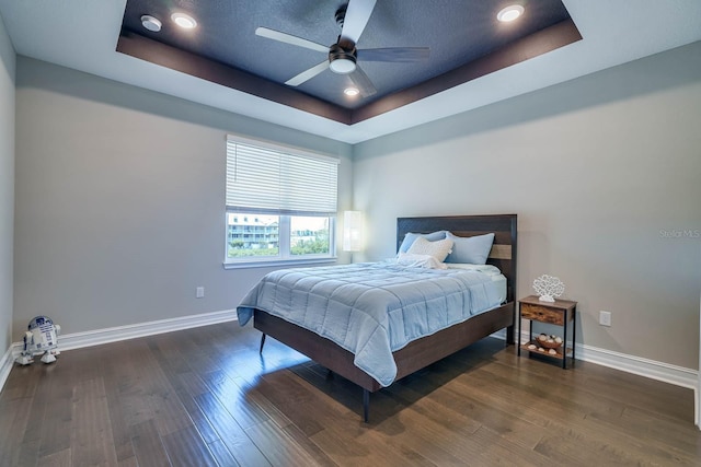 bedroom featuring a raised ceiling, baseboards, wood finished floors, ceiling fan, and recessed lighting