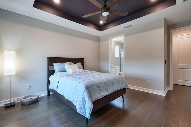 bedroom featuring a tray ceiling, baseboards, dark wood-type flooring, recessed lighting, and ensuite bathroom