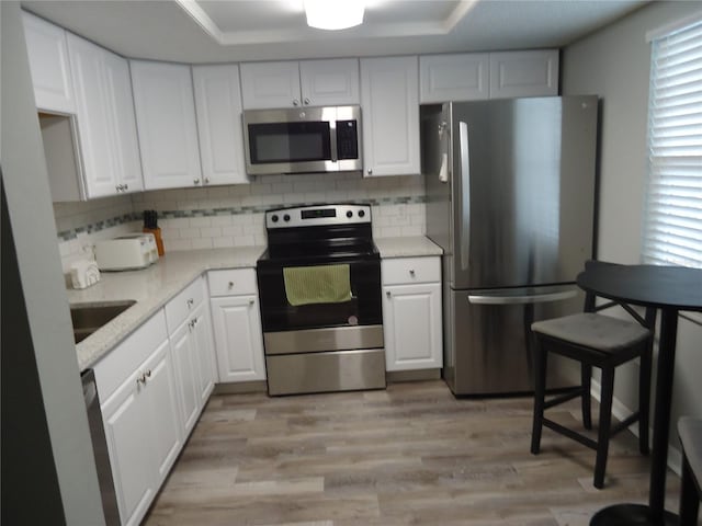 860 Virginia St Unit 308, Dunedin, FL 34698 - kitchen with appliances with stainless steel finishes, white cabinets, decorative backsplash, and light wood-style flooring