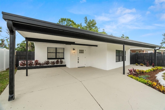 view of front facade with an attached carport, fence, and stucco siding