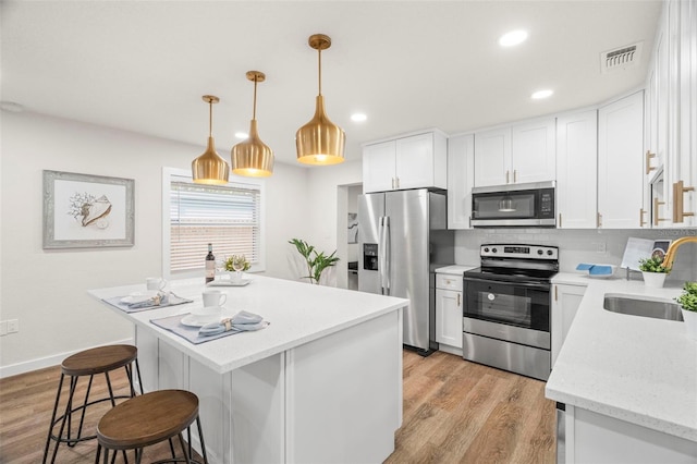 kitchen with appliances with stainless steel finishes, a sink, a kitchen bar, decorative backsplash, and light wood-style flooring