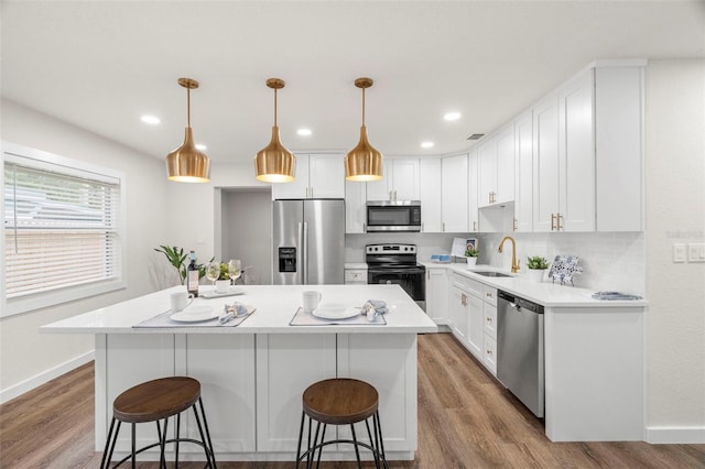 kitchen featuring stainless steel appliances, a sink, a kitchen bar, a kitchen island, and white cabinetry