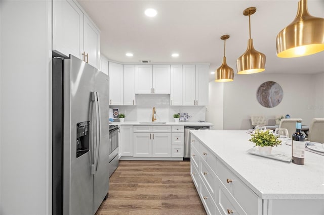 kitchen featuring stainless steel appliances, white cabinets, wood finished floors, a sink, and recessed lighting