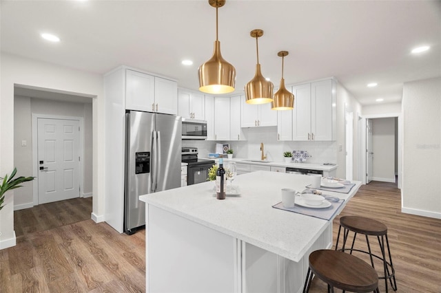 kitchen featuring appliances with stainless steel finishes, a sink, a kitchen bar, white cabinetry, and baseboards