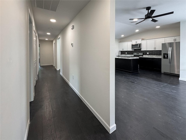 hallway featuring vaulted ceiling, recessed lighting, dark wood finished floors, baseboards, and a sink