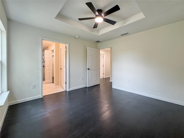 unfurnished bedroom with a raised ceiling, dark wood-type flooring, baseboards, ensuite bath, and ceiling fan