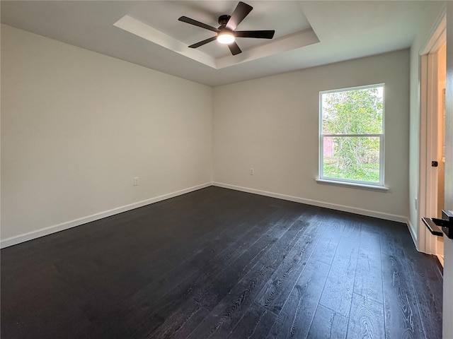 unfurnished room featuring a tray ceiling, dark wood-type flooring, ceiling fan, and baseboards