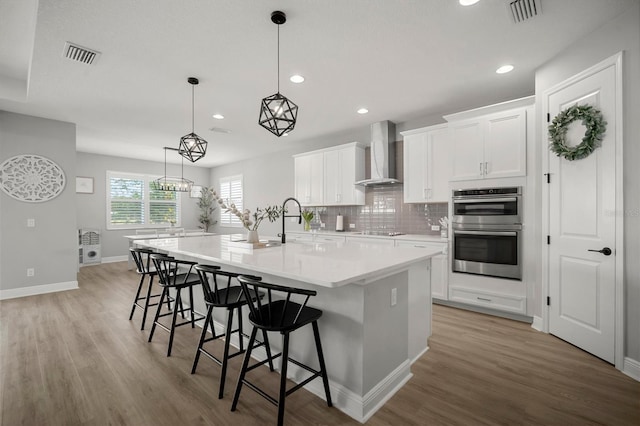 923 Whimbrel Run, Bradenton, FL 34212 - kitchen featuring wall chimney exhaust hood, black electric stovetop, double oven, a large island with sink, and light wood-style flooring
