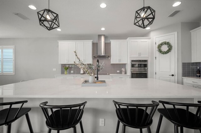 923 Whimbrel Run, Bradenton, FL 34212 - kitchen featuring wall chimney exhaust hood, stainless steel double oven, tasteful backsplash, white cabinetry, and recessed lighting