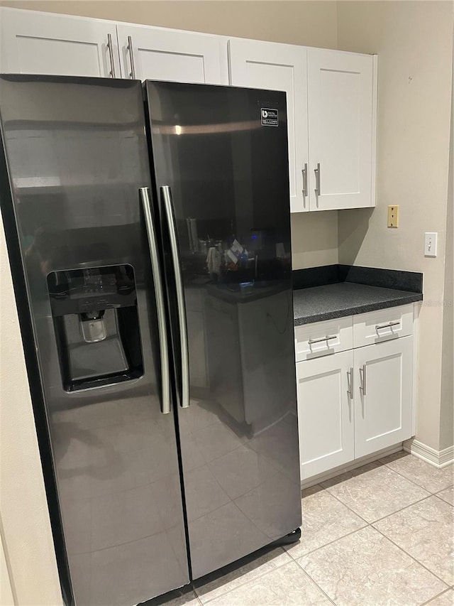 9220 Dayflower Dr, Tampa, FL 33647 - kitchen featuring stainless steel fridge, dark countertops, light tile patterned floors, white cabinets, and baseboards