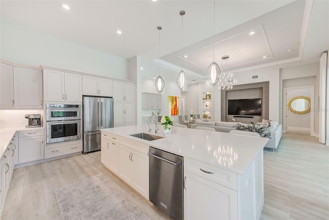 16707 Verona Pl, Bradenton, FL 34202 - kitchen featuring appliances with stainless steel finishes, a tray ceiling, open floor plan, an island with sink, and light wood-type flooring