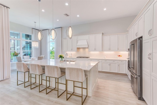 16707 Verona Pl, Bradenton, FL 34202 - kitchen featuring stainless steel appliances, premium range hood, white cabinetry, light countertops, and a kitchen bar