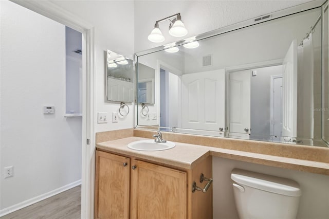bathroom with wood finished floors, toilet, vanity, and baseboards