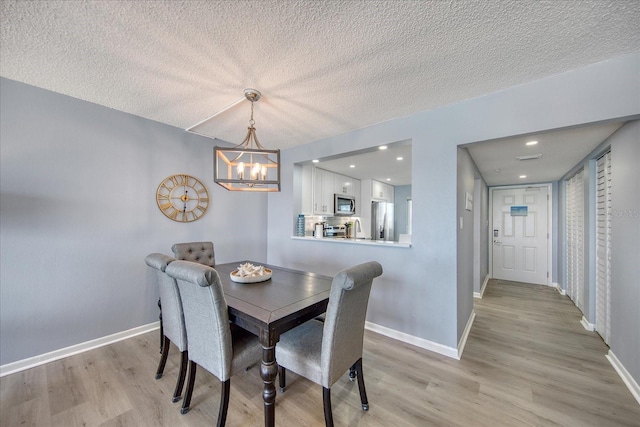 15000 Gulf Blvd Unit 602, Madeira Beach, FL 33708 - dining room featuring a chandelier, a textured ceiling, light wood-type flooring, and baseboards