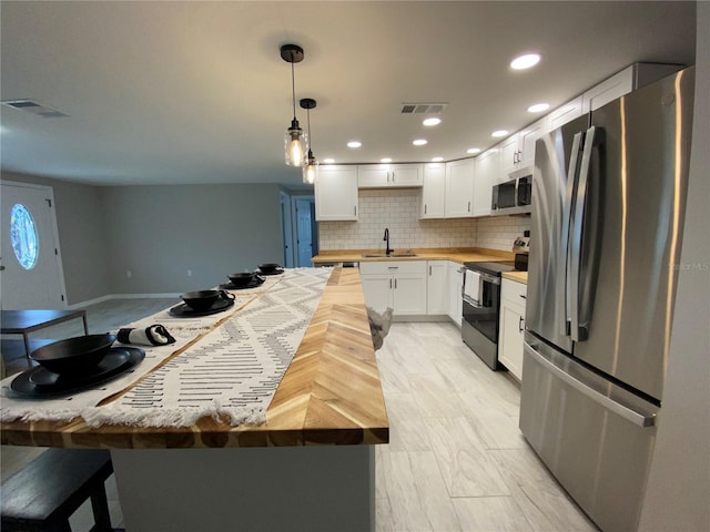 kitchen with appliances with stainless steel finishes, butcher block countertops, a sink, white cabinets, and decorative backsplash