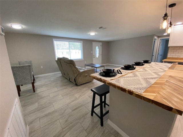 kitchen featuring wooden counters, a breakfast bar area, white cabinetry, hanging light fixtures, and open floor plan