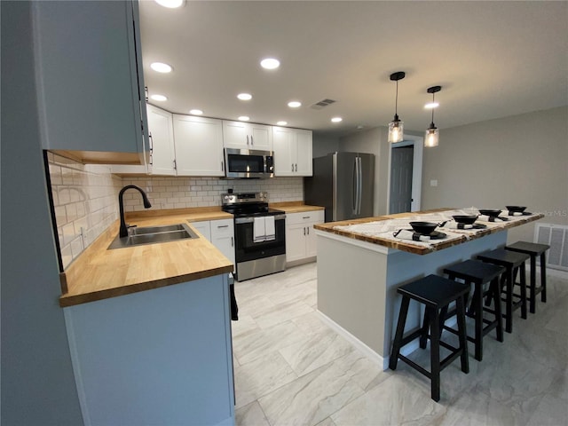 kitchen with stainless steel appliances, wooden counters, a sink, a kitchen bar, and decorative backsplash