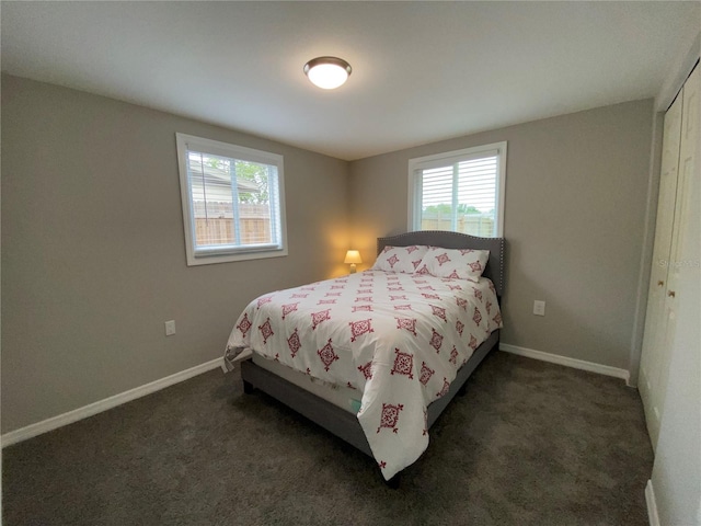 bedroom featuring multiple windows, dark carpet, baseboards, and a closet