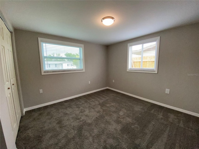 unfurnished bedroom with dark colored carpet, a closet, and baseboards