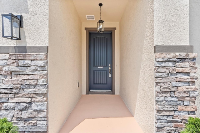 doorway to property featuring stucco siding and stone siding